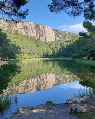 Serene lake reflecting mountains and trees under a clear sky.