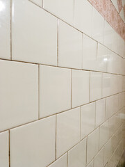 A white tiled wall in a bathroom with a pink and white tile border
