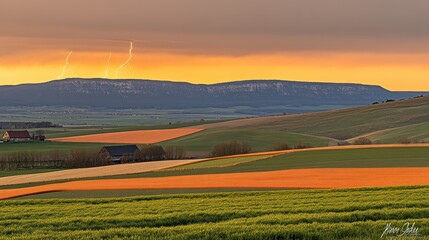 Obraz premium Dramatic sunset over rolling hills with colorful fields and storm clouds.
