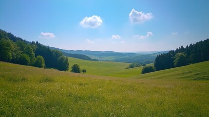 Obraz premium A serene landscape with rolling hills, green fields, and a clear blue sky.