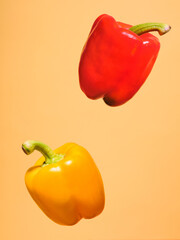 Two peppers, one yellow and one red, floating in the air against a yellow background. Captured in a...