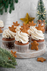 Christmas gingerbread cupcakes with cream cheese frosting and mini gingerbread cookies on top on a wooden board. Festive dessert.