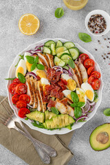 Healthy cobb salad with roasted chicken breast, chopped avocado, tomatoes, bacon, cucumber, hard boiled egg and green leaves on a plate. Top view.