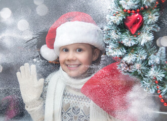 little girl in santa hat and with gifts shines a lantern into the window from winter street