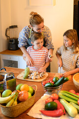 A brother and sister help their mother in the kitchen, chopping mushrooms, cucumbers, and tomatoes....