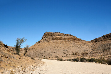 Dirt road between desert hills against a blue sky. Desert landscape and environment