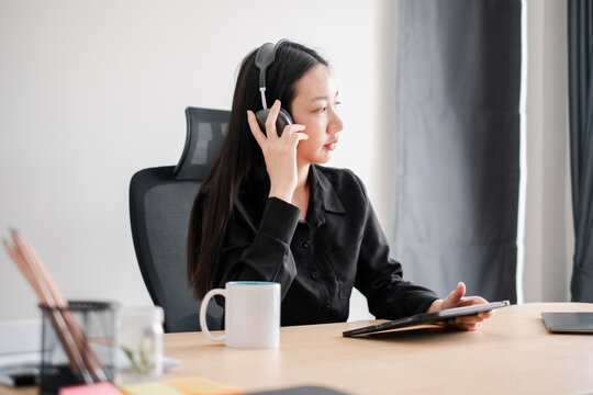 Professional woman in a modern office setting, using a tablet and headphones for remote work and communication. - Powered by Adobe