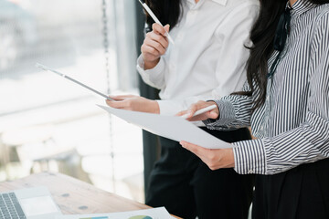 Two business professionals reviewing documents and digital tablets in a bright, modern office...