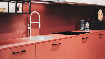 A kitchen with a red countertop and black handles on the cabinets. A sink is located on the countertop
