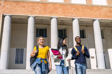Obraz premium Multiethnic students walking down university steps on a sunny day
