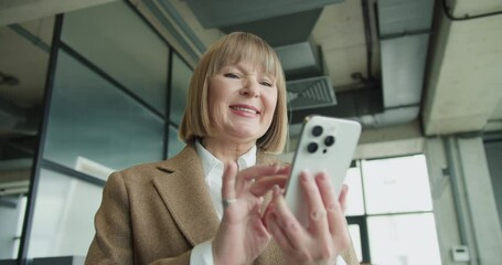 A mature businesswoman using a smartphone in a modern office environment, focusing on professional tasks or communication, highlighting confidence and technological proficiency