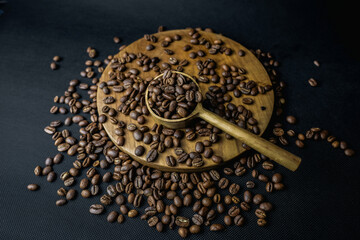 Close-up of roasted coffee beans in a wooden spoon on a rustic wooden plate isolated on a black...