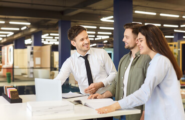 Young caucasian couple standing at building market or big shopping mall with male friendly salesman...