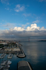 Obraz premium Lisbon cityscape with 25 de abril bridge over tagus river under cloudy sky