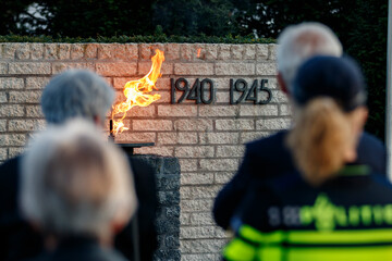 Memorial flames burn at a 1940-1945 war memorial.  Attendees stand in remembrance.