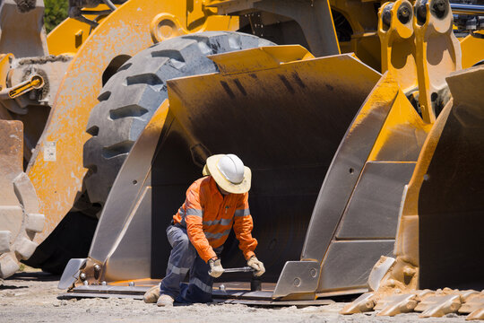 Man tightening the bolts on the bucket of a payloader.