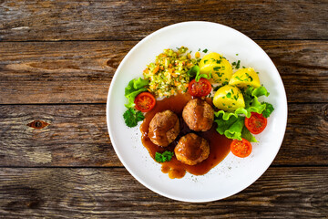 Seared pork meatballs with sauce, boiled potatoes and cabbage salad on wooden table	