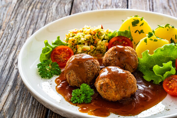 Seared pork meatballs with sauce, boiled potatoes and cabbage salad on wooden table	