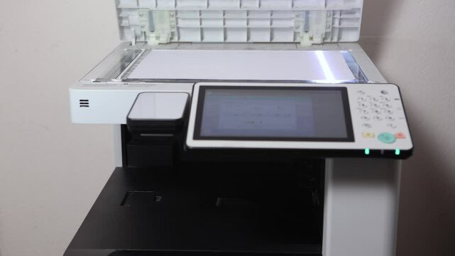 An office worker scans an A3 sheet of paper on a scanner. A man's hand presses a button to scan or copy a document on an office MFP.