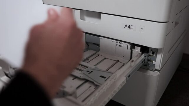 An office worker takes out a stack of paper from the printer tray. A man's hand takes a stack of A3 sheets of paper from an office MFP.