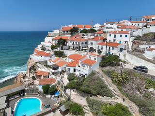 Obraz premium A picturesque village perched on a cliff overlooking the ocean with a sparkling pool in the foreground