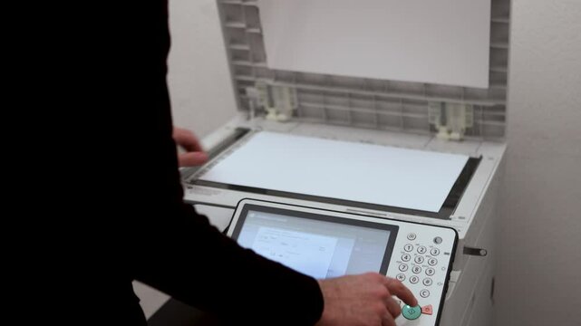 An office worker scans an A3 sheet of paper on a scanner. A man's hand presses a button to scan or copy a document on an office MFP.