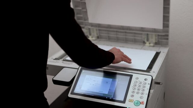 An office worker scans an A3 sheet of paper on a scanner. A man's hand presses a button to scan or copy a document on an office MFP.