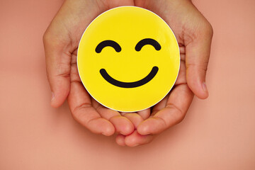 Hands holding a happy smiling face in yellow. Concept for positive customer satisfaction reviews, mental health, compliments, world mental health day