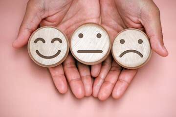 Hand holding a sad face, flat face, happy face carved on wood. Mental health concept, split...