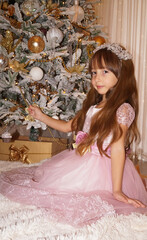 beautiful little girl looks like queen near the christmas tree