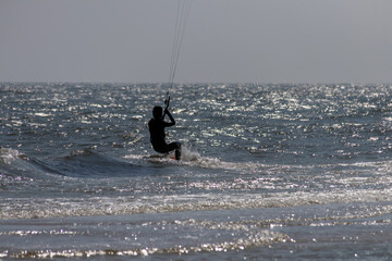 A silhouette of a kite surfer gracefully riding the waves under a shimmering sky