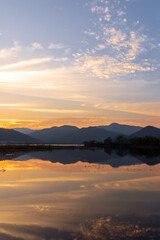 Fototapeta premium Serene sunset over a tranquil lake, with vibrant colors reflecting on the water and mountains in the background.