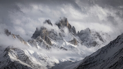 Obraz premium A breathtaking mountainous landscape with jagged snow-covered peaks shrouded in mist and clouds creating a serene ethereal atmosphere dominated by shades of white and gray with peaks 