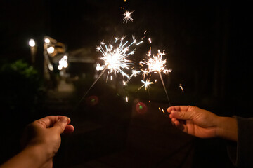 Two hands hold sparklers, illuminating the dark night with sparkling light