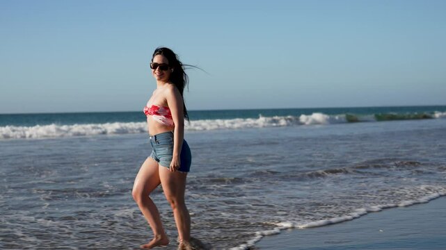 Beautiful latin woman walking on the beach and listening to music, summer and vacation concept