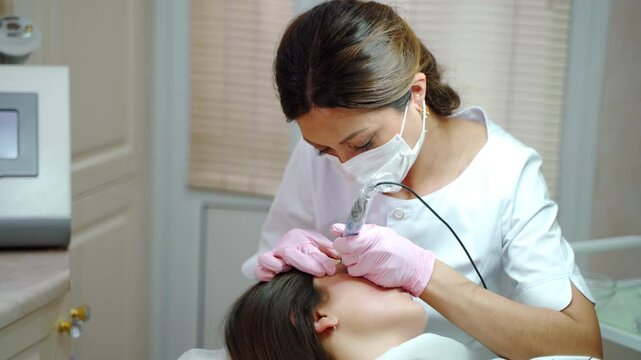 Female brow master uses needle ink machine. Procedure of permanent make up in salon.