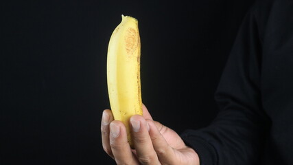 Male hands holding the banana on black background.