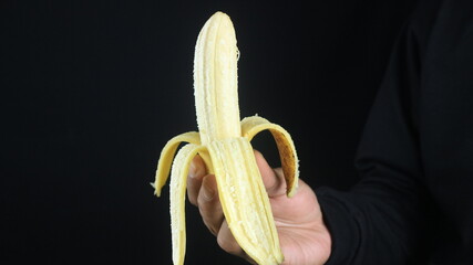 Male hands holding the banana on black background.