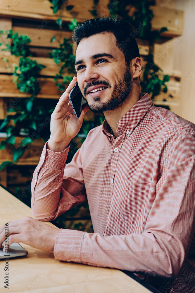 Poster smiling handsome man having telephone conversation during remote job via laptop computer, cheerful h