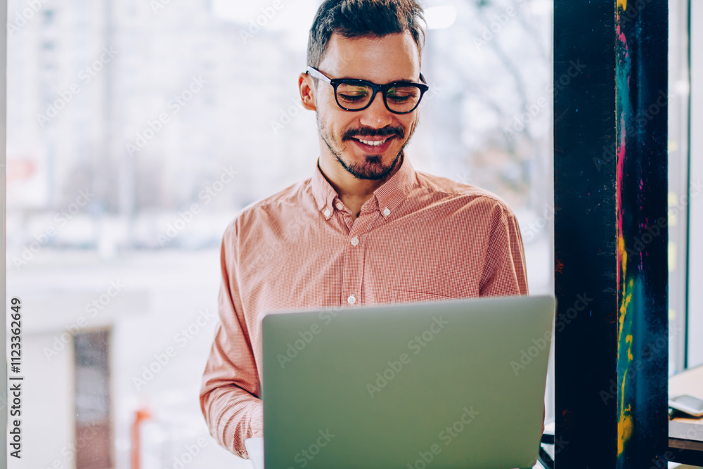 Poster young hipster guy satisfied with spectacles for vision protection reading information from laptop co