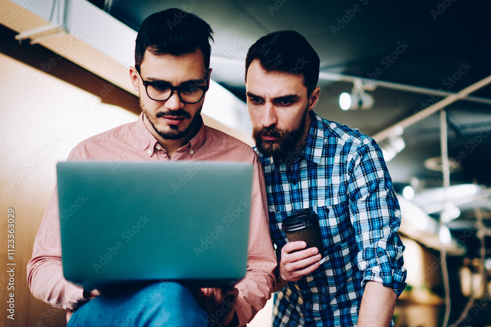 Poster serious male coworkers concentrated on fixing bugs of application on laptop computer looking togethe