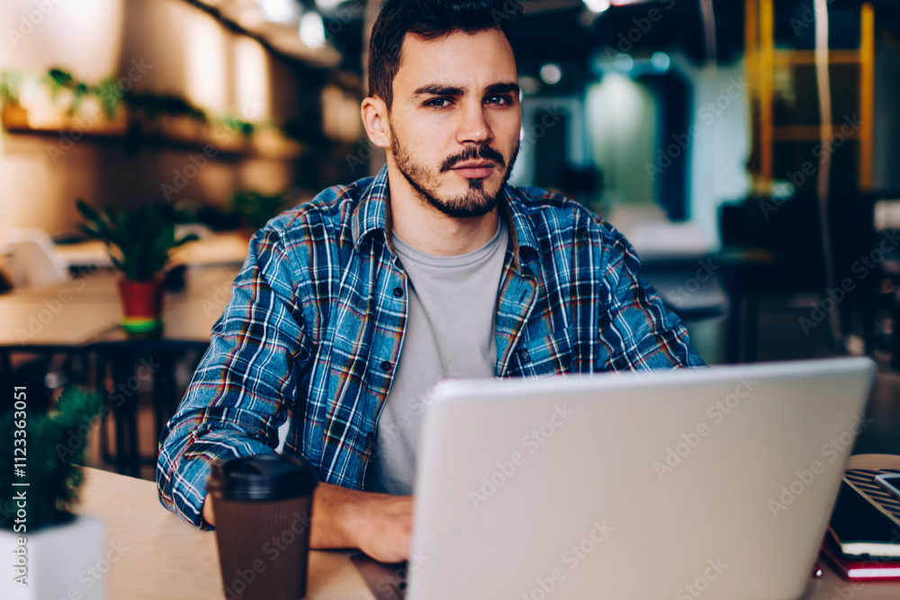 Poster portrait of serious hipster guy making research for exam preparation using netbook and wifi in colle