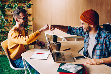 Prosperous male it developers clinking fists in sign of agrement cooperating on common startup...