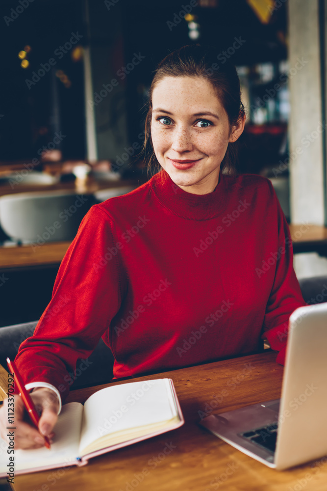 Poster portrait of surprised skilled student smiling at camera and making notes in notebook preparing for e