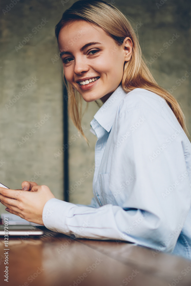 Poster portrait of happy hipster girl smiling at camera while installing mobile application on smartphone d