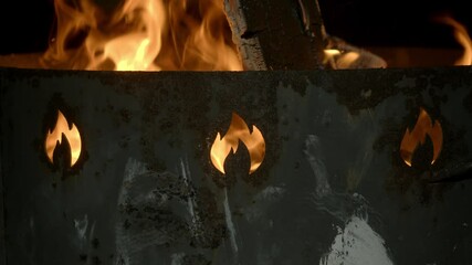 A bonfire is burning in an old, rusty metal brazier, with holes shaped like a flame. Close up. - Powered by Adobe