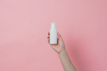 White unbranded cream bottle with pump in hand on pink background. Concept of beauty. Product cosmetic advertising