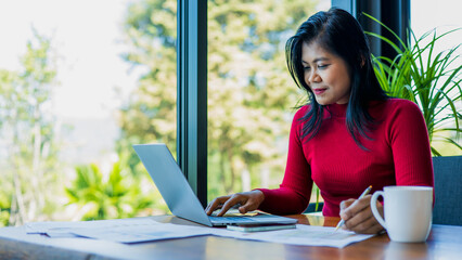 Woman working using laptop online meeting in home office, Business women wearing red sweater...