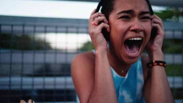 close-up of dark-skinned African American woman feeling stees, screaming in emotional agony while holding her headphones. raw vulnerability, showcasing intense frustration, pain, and inner turmoil
