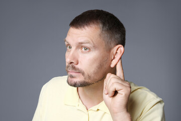Man showing hand to ear gesture on grey background